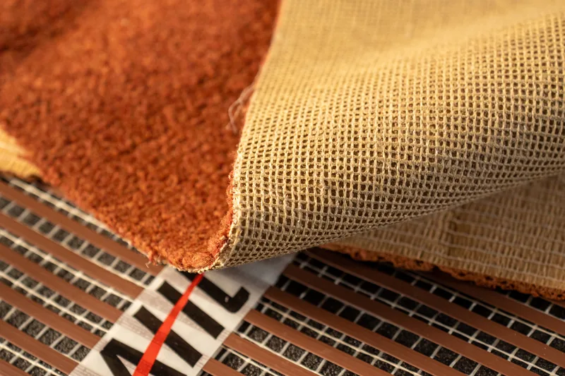 Carpet sample curled back to show its woven backing above heating ribbon.