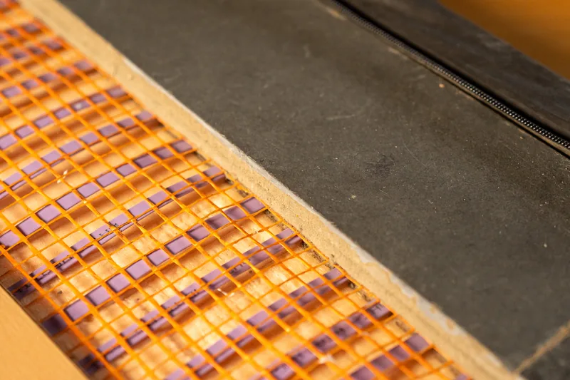 Dark flooring sample with its pale core visible above orange-mesh heating.