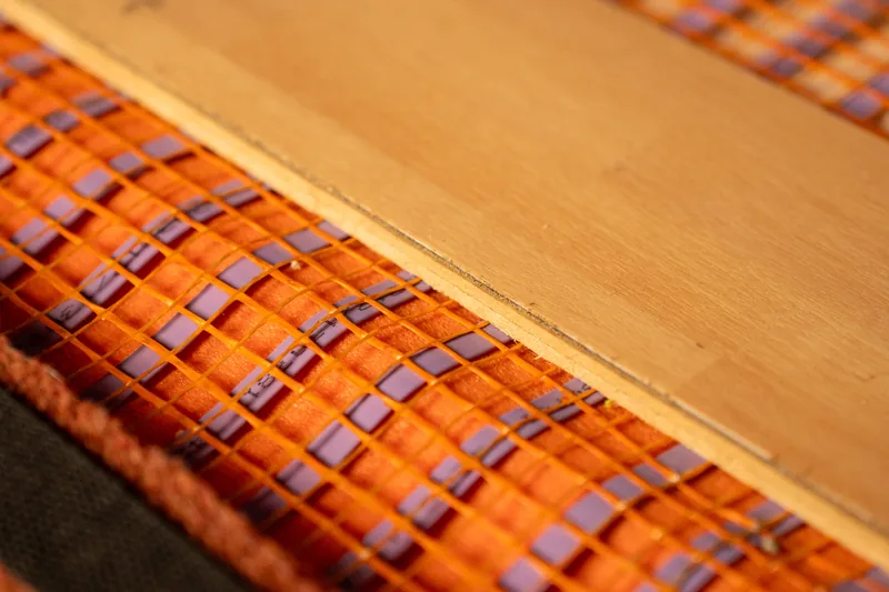 Pale wood-effect flooring sample above an orange-mesh heating mat.