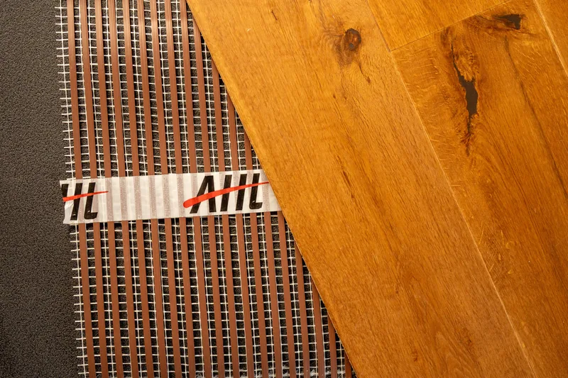 Golden wood-effect flooring sample with visible knots beside heating ribbon.