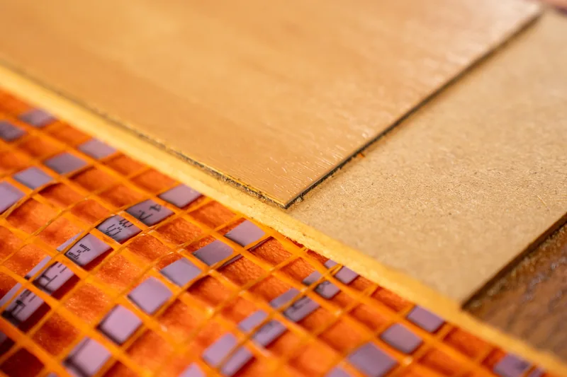 Layered flooring sample above an orange-mesh underfloor heating sample.