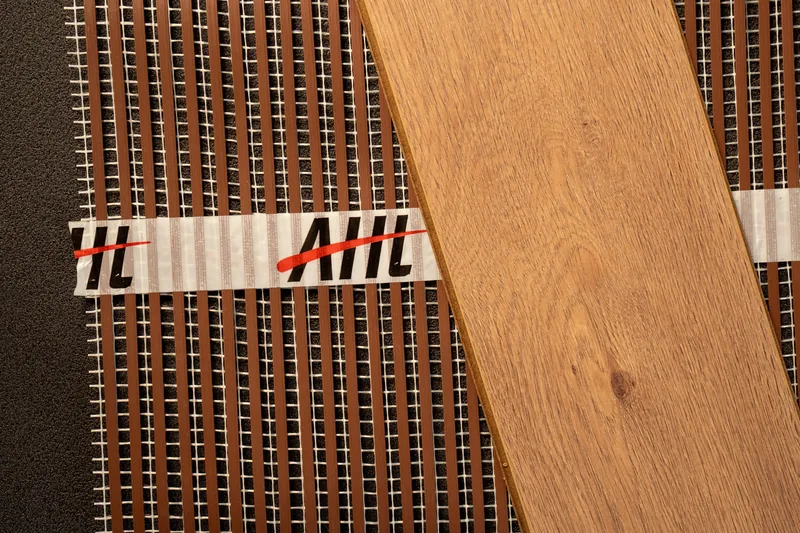 Light wood-effect flooring sample laid across a ribbon heating mat.